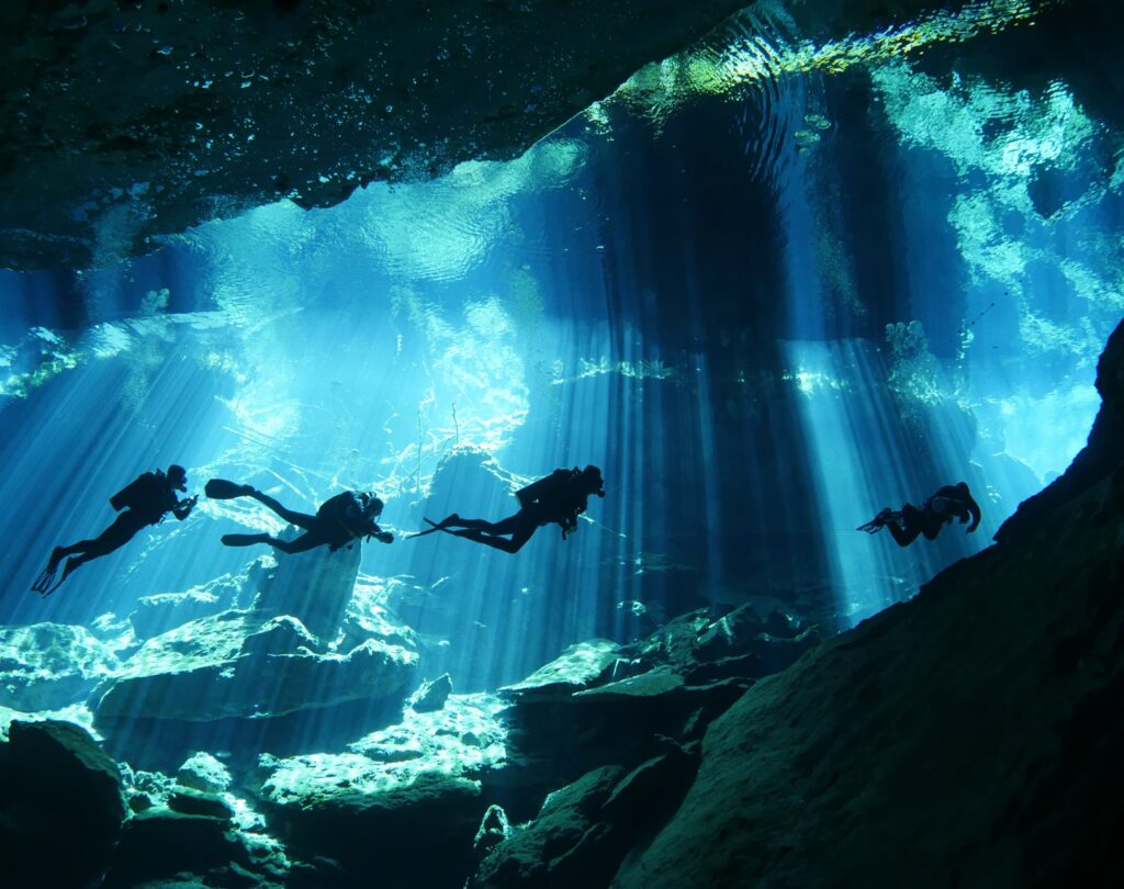 Plongeurs en exploration dans le cénote Chac Mool avec rayons de lumière sous-marins