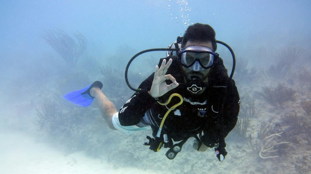 pexels photo 4765931 4765931 Scuba diver underwater making an okay sign while exploring the seabed with corals.