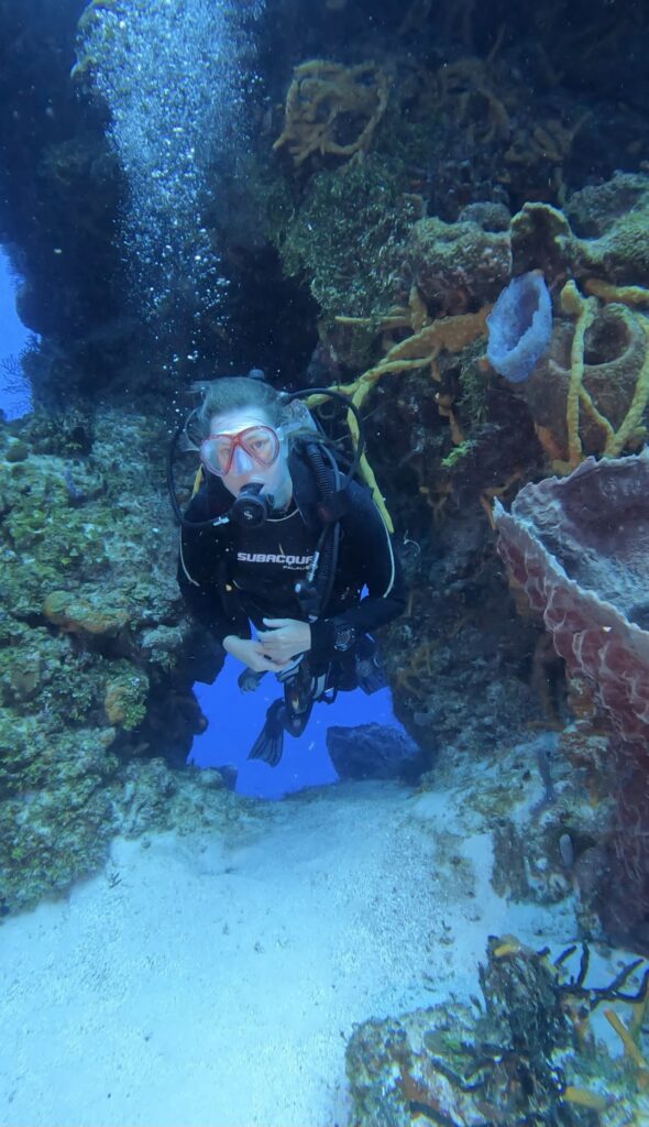 Plongée loisir à Cozumel : explorer différents environnements Plongeuse en plongée loisir traversant un petit tunnel sur un récif de Cozumel, au Mexique, lors d'une plongée d'exploration.