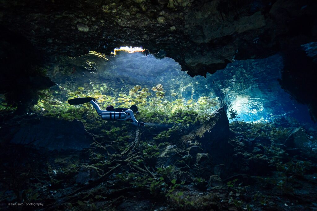 Zone cavern d'un cénote au Mexique avec la sortie visible et des rayons de lumière traversant l'eau cristalline.